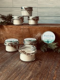 three jars with candles sitting on top of a wooden table next to evergreen branches and pine cones