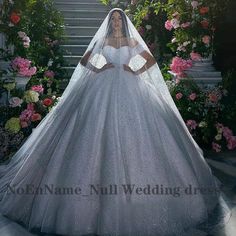 a woman in a white wedding dress and veil with flowers on the stairs behind her