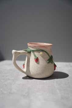 a ceramic mug with strawberries on it sitting on top of a cement tablecloth