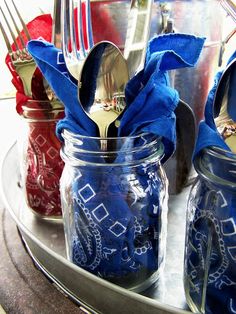 three jars with spoons, forks and napkins in them on a metal tray