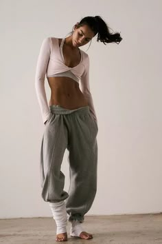 a woman standing in front of a white wall wearing sweat pants and a crop top