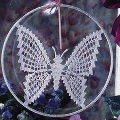 a glass ornament with a white butterfly on it and purple flowers in the background