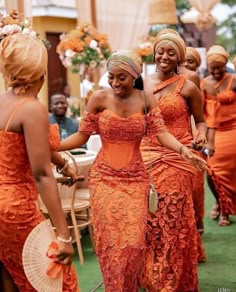 two women in orange dresses walking down the aisle with other people behind them wearing head wraps