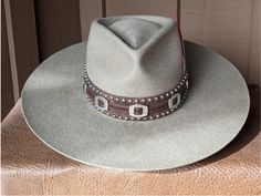 The Bandit is a stand out hat that captures the feeling of the American West. . The base of the hatband is distressed leather that is then layered with imprinted brown leather, bolo sliders and lots of nailspots. It is finished with this colorful feather combo. The brim of the LID custom hat body is 4" in diameter and the crown is 4.5". This is a stiff hat. Available in Putty or Pecan All hats are made to order. Allow up to 4 weeks for your hat to ship. Distressed Brown Hats With Short Brim For Country Events, Distressed Brown Brimmed Hat, Western Hats With Distressed Brown Short Brim, Distressed Brown Western Hat With Short Brim, Distressed Brown Hat For Rodeo, Distressed Brown Hat For Country Events, Distressed Brown Rodeo Hat With Short Brim, Western Distressed Brown Hat, Distressed Brown Short Brim Hat For Rodeo