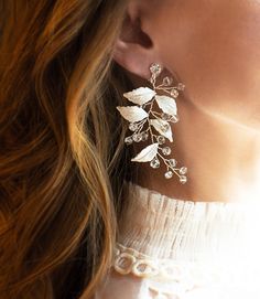 a close up of a woman's ear wearing earrings with leaves and pearls on them