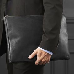 a man in a suit holding a black leather briefcase with his hand on the other side