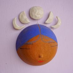 an orange with blue hair and three moon faces on it's face is hanging from the wall