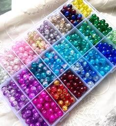 many different colors of beads in a plastic container on a lace tablecloth with white lacy material