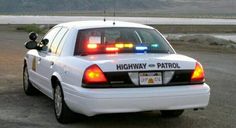 the police car is parked on the side of the road by the water and mountains