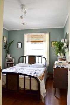 a bed room with a neatly made bed next to a window and a potted plant