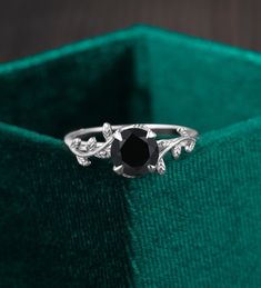 a black diamond ring sitting on top of a green velvet box with leaves around it