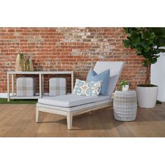 a white chaise lounge chair sitting in front of a brick wall and potted plant