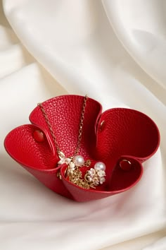 a red leather jewelry box with pearls and chains on white silk background, closeup