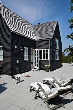 a black house with two lawn chairs and a dog on the ground in front of it