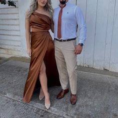 a man and woman standing next to each other in front of a white wall wearing brown dresses