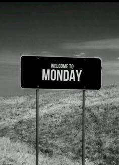 a sign that says welcome to monday on it in front of a grassy hill and blue sky