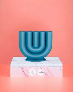 a blue vase sitting on top of a marble block in front of a pink wall