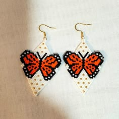 two orange and black butterfly shaped beaded earrings on white fabric with gold colored hooks