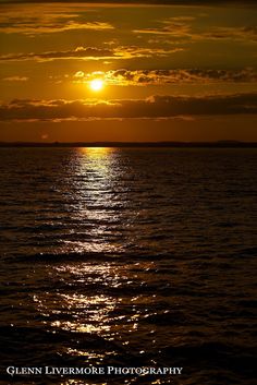 the sun is setting over the ocean with clouds in the sky and reflecting on the water