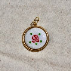 a red rose embroidered onto a gold frame on a white fabric background with green leaves