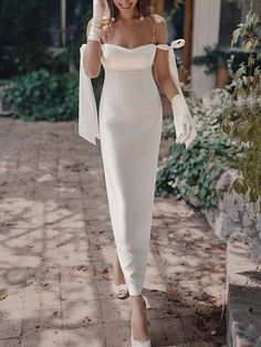 a woman in a white dress and gloves walking down the street with her hand on her head