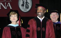 three people standing in front of a sign at graduation