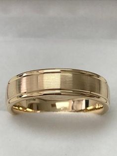 a yellow gold wedding ring on a white surface with the band slightly curled up to it's sides