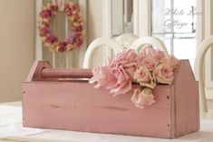 a pink wooden box with flowers in it on a table next to chairs and wreath