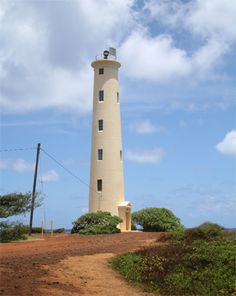 a white light house sitting on top of a dirt hill next to trees and bushes