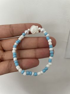 a white and blue beaded bracelet with a seashell charm on it's end