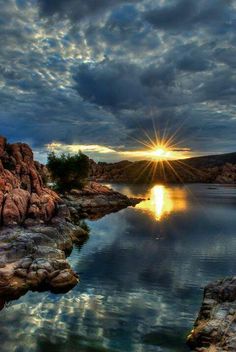 the sun shines brightly through the clouds over a body of water surrounded by rocks