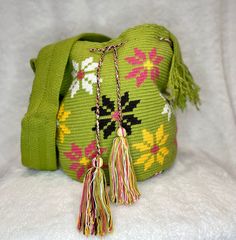 a green purse with tassels and flowers on the front is sitting on a white surface