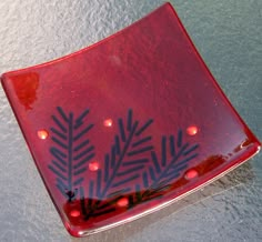 a red plate with black designs on it sitting on top of a table next to water