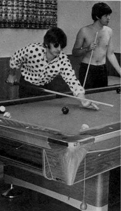 two men are playing pool in an old black and white photo with one man leaning over the table