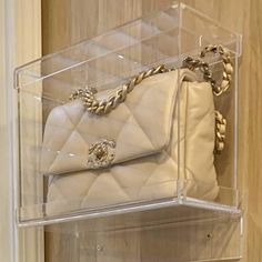 a white purse sitting inside of a clear case on top of a shelf next to a wall