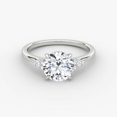 a white gold engagement ring with three stones on the side and a round brilliant diamond center