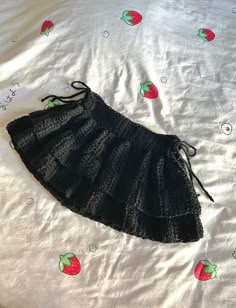 a black crocheted skirt laying on top of a white bed sheet with strawberries drawn on it