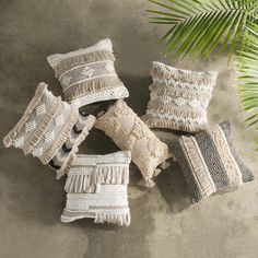 four pillows with fringes on them sitting next to a palm tree