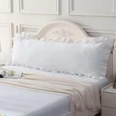 a white bed topped with pillows next to a night stand