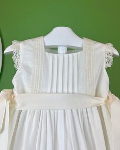 A gorgeous off-white dress for special occasions, made with a lightweight linen fabric and laces. It has buttons on the back for closure and satin strings to form two bows on the sides. Dry clean Made in Spain Final Sale, no exchanges nor returns are accepted White Spring Dress With Satin Bow, White Spring Dresses With Satin Bow, White Satin Bow Dress For Spring, White Dresses With Satin Bow For Spring, White Sleeveless Dress For Ceremony, White Wedding Dress With Ribbon Detail, Summer Baptism Dress With Bow, White Sleeveless Linen Dress With Tie Back, Elegant Cream Baptism Dress For Summer