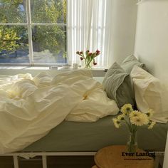 an unmade bed in front of a window with white sheets and pillows on it