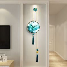 a clock with tassels hanging from it's side on the wall next to a tv