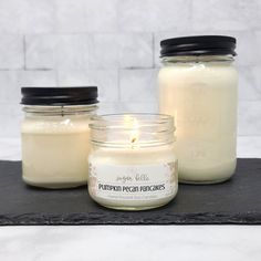 three jars filled with candles sitting on top of a black slate tray next to each other