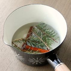 a pot filled with carrots and herbs on top of a wooden table next to a knife