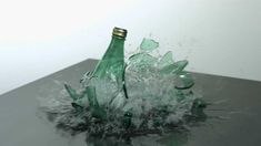 two green bottles with water splashing out of them on top of a black table