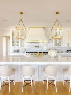 a large kitchen with white cabinets and gold accents on the hood over the stove is surrounded by three stools