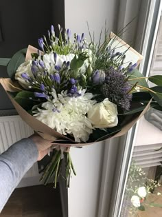 a person holding a bouquet of white and purple flowers in front of an open window