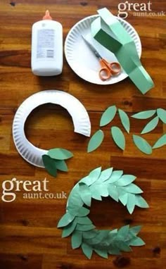 paper plate wreaths, scissors and glue sitting on a wooden table with green leaves