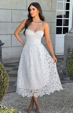 a woman standing in front of a building wearing a white dress with lace on it