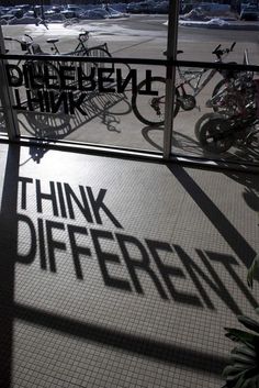 the shadows of bicycles are cast on the floor in front of a glass window that reads think different